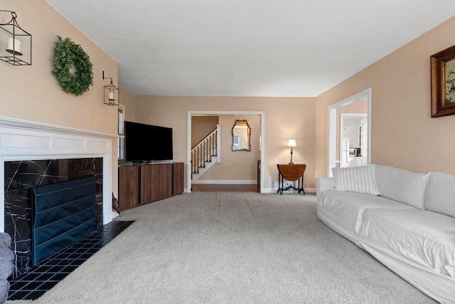 carpeted living room with stairs, a premium fireplace, and baseboards