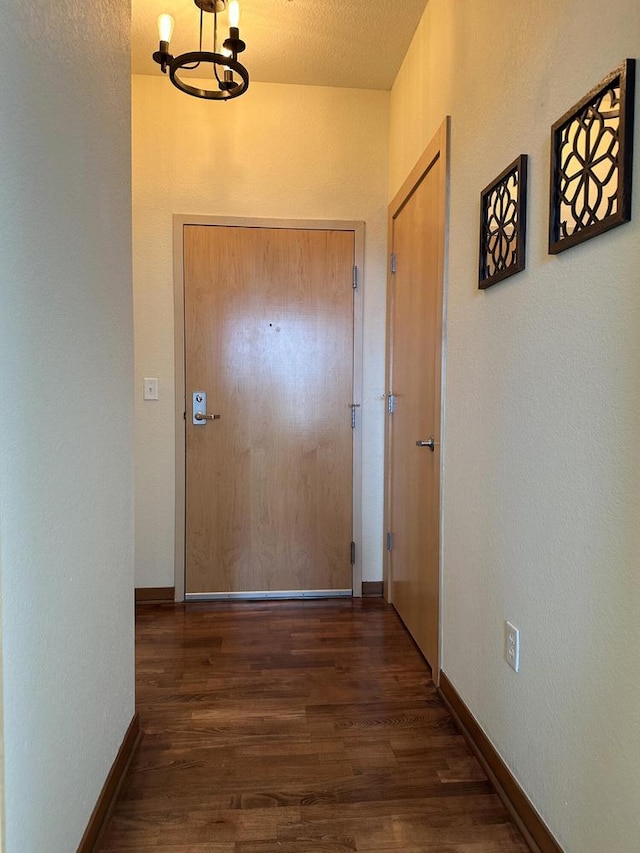 corridor with baseboards, wood finished floors, and a chandelier