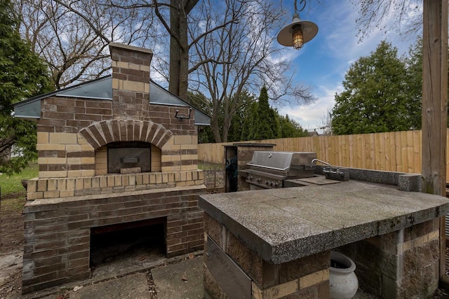 view of patio with fence, grilling area, exterior kitchen, an attached garage, and an outdoor brick fireplace