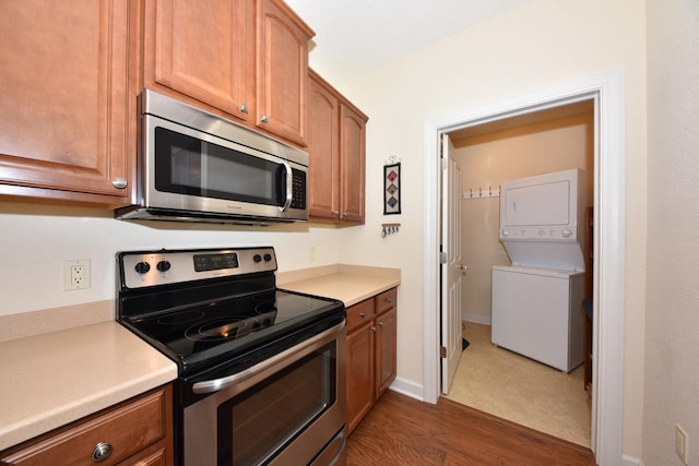 kitchen featuring light countertops, brown cabinets, dark wood finished floors, appliances with stainless steel finishes, and stacked washer / drying machine