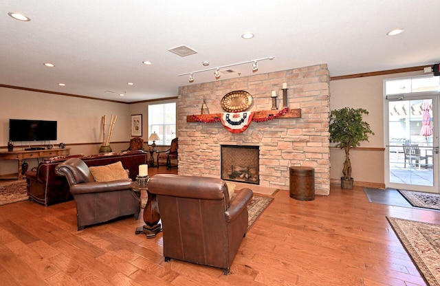 living area featuring a stone fireplace, visible vents, crown molding, wood finished floors, and baseboards