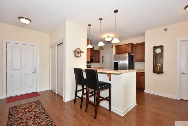kitchen with light countertops, a kitchen breakfast bar, stainless steel fridge, and dark wood-type flooring