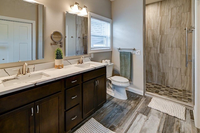 bathroom featuring toilet, tiled shower, a sink, and wood finished floors