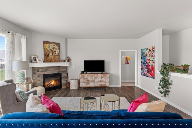living room featuring baseboards, a stone fireplace, and wood finished floors