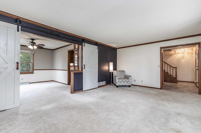 unfurnished room with a barn door, carpet floors, baseboards, visible vents, and ornamental molding