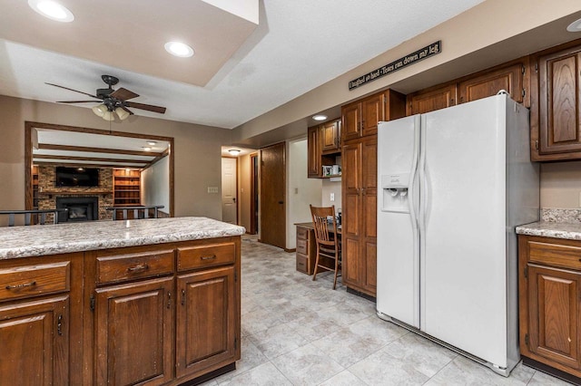kitchen with white refrigerator with ice dispenser, a fireplace, light countertops, a ceiling fan, and recessed lighting