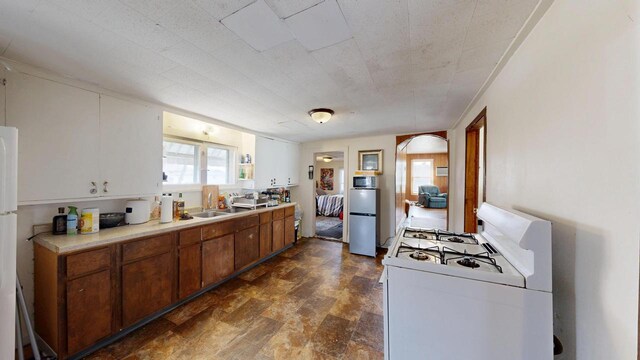 kitchen with refrigerator, light countertops, white range with gas cooktop, arched walkways, and a sink
