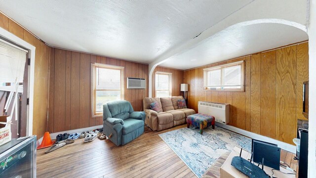 living room featuring wooden walls, arched walkways, a wall mounted AC, and hardwood / wood-style floors