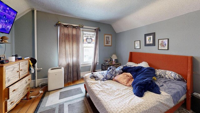 bedroom with a textured ceiling, baseboards, vaulted ceiling, and wood finished floors