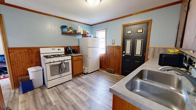 kitchen with white appliances, wooden walls, wainscoting, and a sink