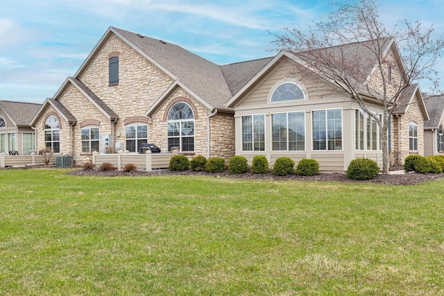 rear view of house featuring a lawn, cooling unit, and stone siding