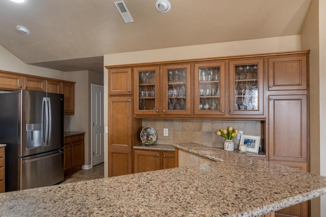 kitchen featuring brown cabinets, light stone counters, glass insert cabinets, and stainless steel fridge with ice dispenser