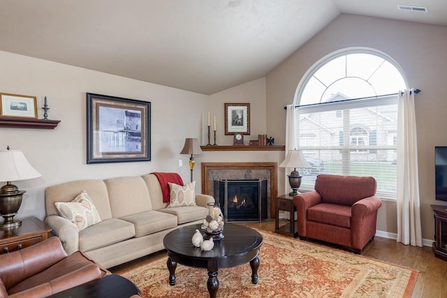 living area featuring visible vents, light wood-type flooring, a tile fireplace, and lofted ceiling