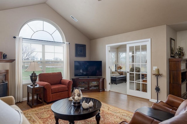 living area with visible vents, baseboards, wood finished floors, and vaulted ceiling