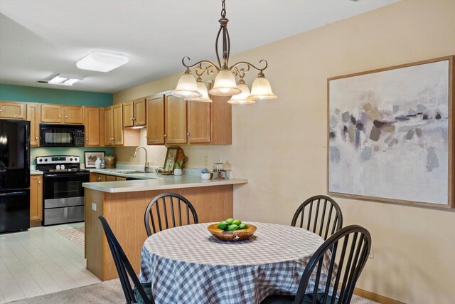 kitchen with pendant lighting, a peninsula, light countertops, a sink, and black appliances
