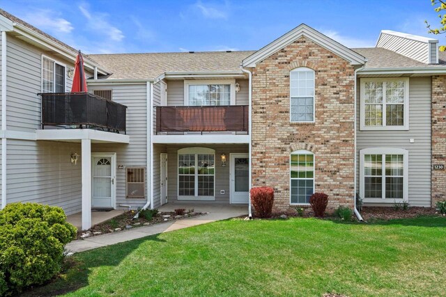 rear view of property featuring a lawn, brick siding, and a balcony
