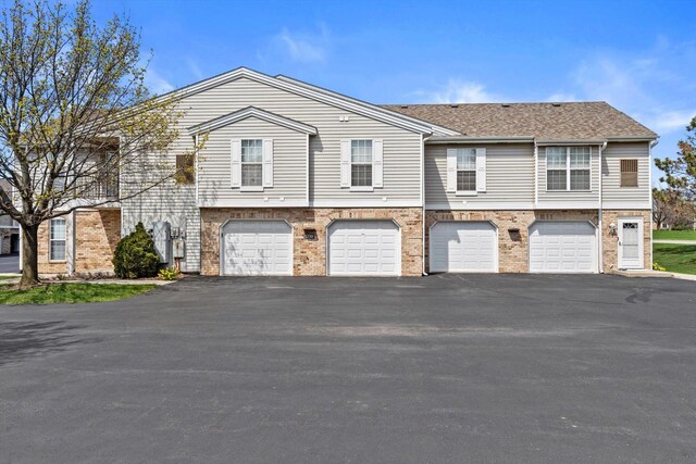 townhome / multi-family property featuring brick siding, a garage, driveway, and a shingled roof