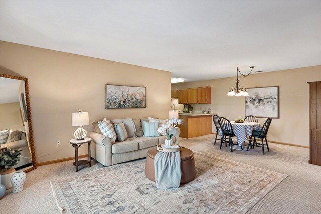 living area with baseboards, a notable chandelier, and light carpet