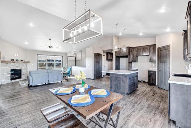 dining room featuring wood finished floors, a ceiling fan, a glass covered fireplace, and lofted ceiling
