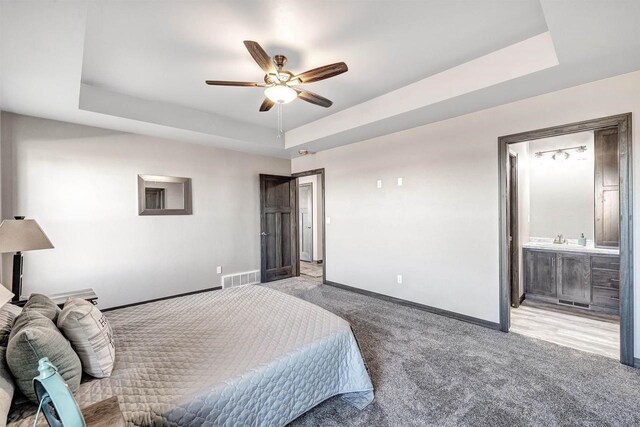 bedroom featuring a sink, carpet, baseboards, a tray ceiling, and visible vents