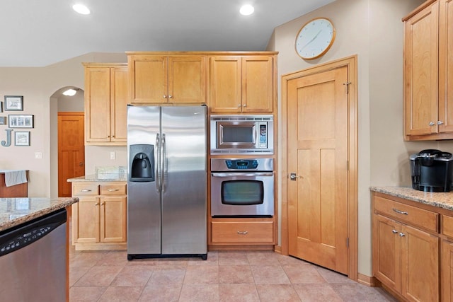kitchen with stainless steel appliances, light stone countertops, arched walkways, and light brown cabinets