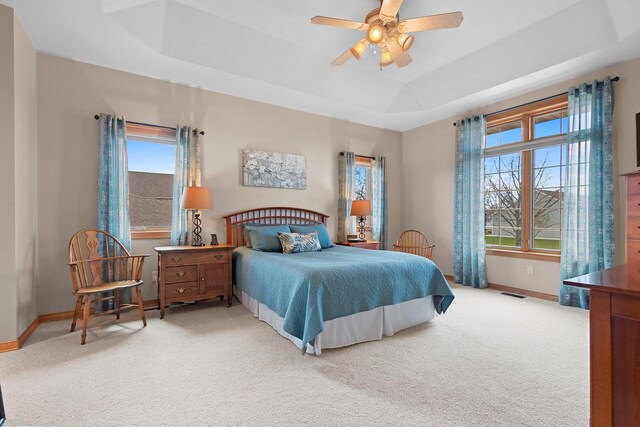bedroom featuring a tray ceiling, visible vents, light carpet, and baseboards