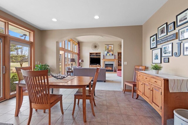 dining area featuring arched walkways, a glass covered fireplace, recessed lighting, baseboards, and light tile patterned floors