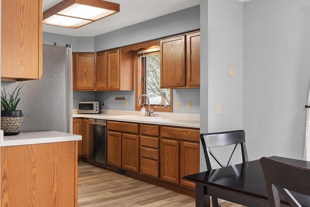 kitchen featuring brown cabinetry, dishwasher, a sink, light countertops, and light wood finished floors