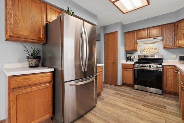 kitchen featuring brown cabinets, appliances with stainless steel finishes, light wood-style floors, light countertops, and under cabinet range hood
