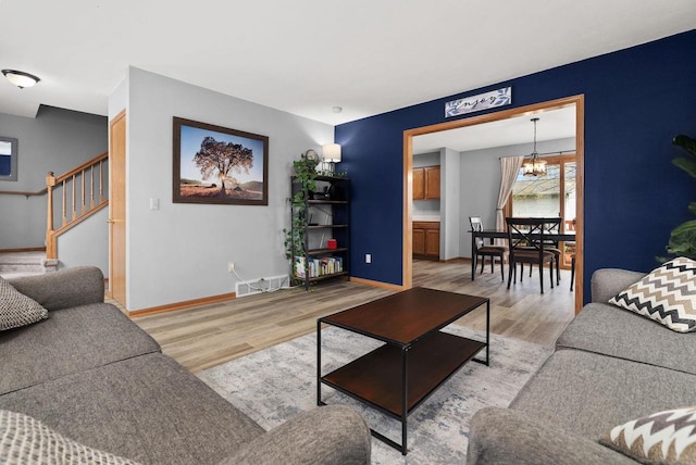 living room with stairs, baseboards, a chandelier, and light wood-type flooring