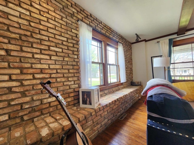 interior space featuring brick wall, visible vents, a wealth of natural light, and hardwood / wood-style flooring