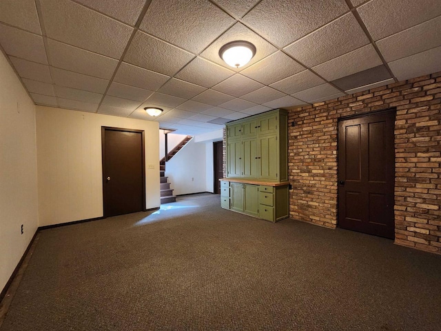 finished basement with dark carpet, a paneled ceiling, brick wall, and stairway