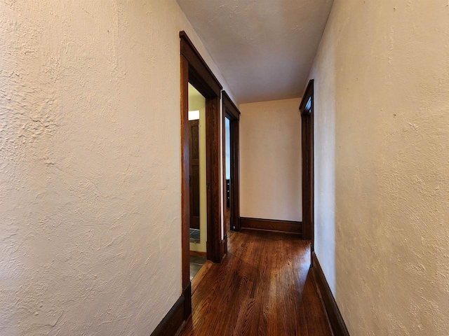 hallway featuring baseboards, a textured wall, and wood finished floors