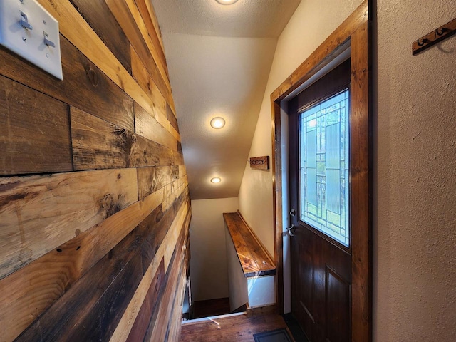 corridor with wooden walls, wood finished floors, and lofted ceiling