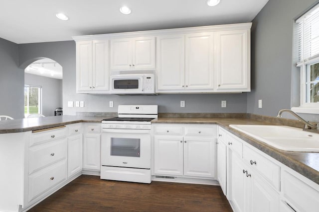 kitchen with a peninsula, white appliances, arched walkways, white cabinets, and a sink