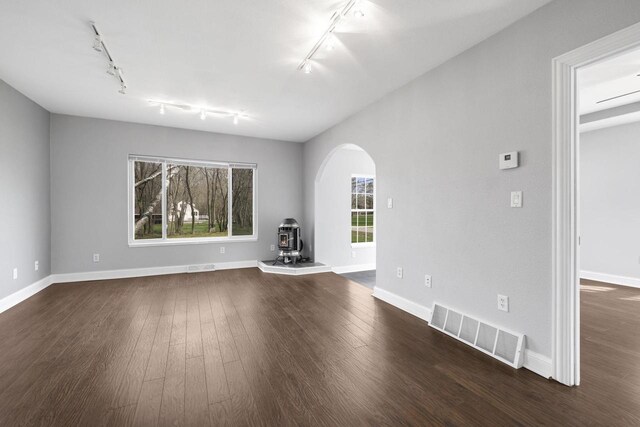 unfurnished living room featuring arched walkways, rail lighting, visible vents, and a wood stove