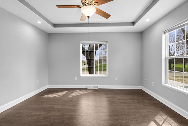 unfurnished room with a tray ceiling, visible vents, dark wood-style floors, and a healthy amount of sunlight