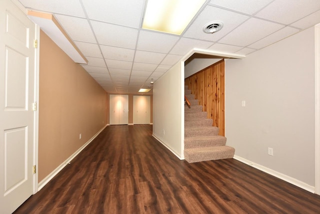 finished below grade area featuring a drop ceiling, stairs, wood finished floors, and visible vents