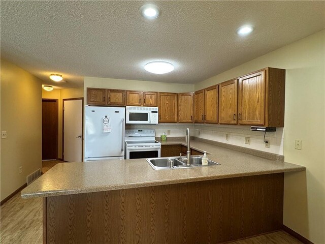 1140 W Hamilton Ave Unit 1140, Eau Claire, WI 54701 - kitchen featuring brown cabinets, a sink, white appliances, a peninsula, and visible vents