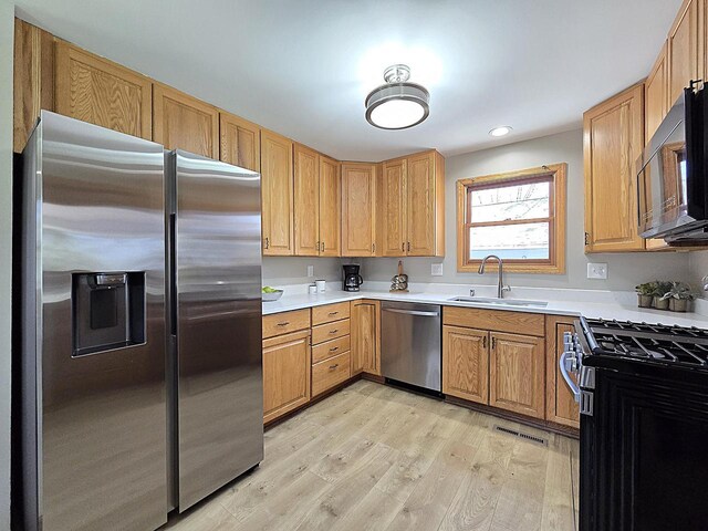 kitchen featuring appliances with stainless steel finishes, light wood-type flooring, a sink, light countertops, and recessed lighting