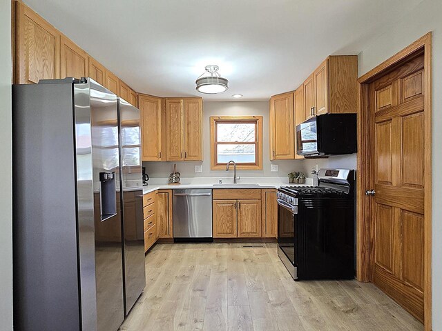kitchen with light countertops, stainless steel appliances, a sink, and light wood-style floors