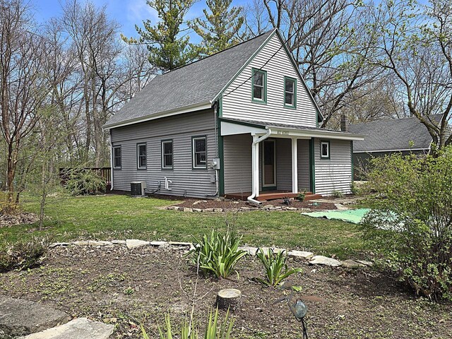 view of front of home with a porch, central AC unit, roof with shingles, and a front yard