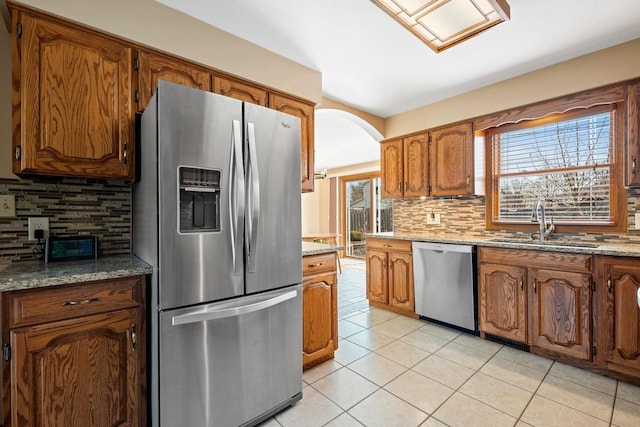 kitchen with brown cabinets, appliances with stainless steel finishes, a sink, decorative backsplash, and light tile patterned floors