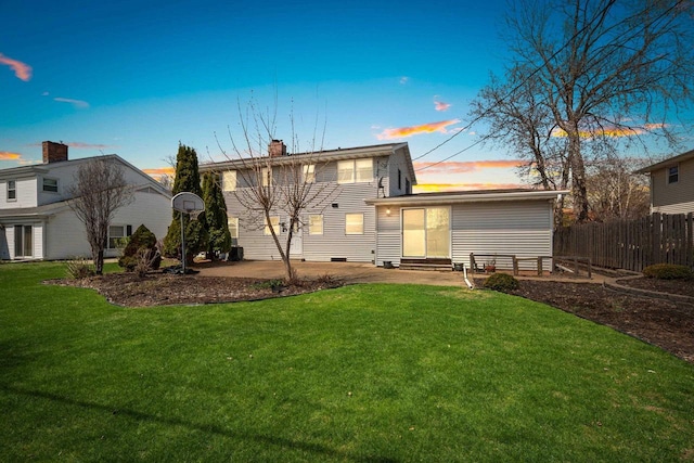back of property at dusk with fence, entry steps, a chimney, a patio, and a yard