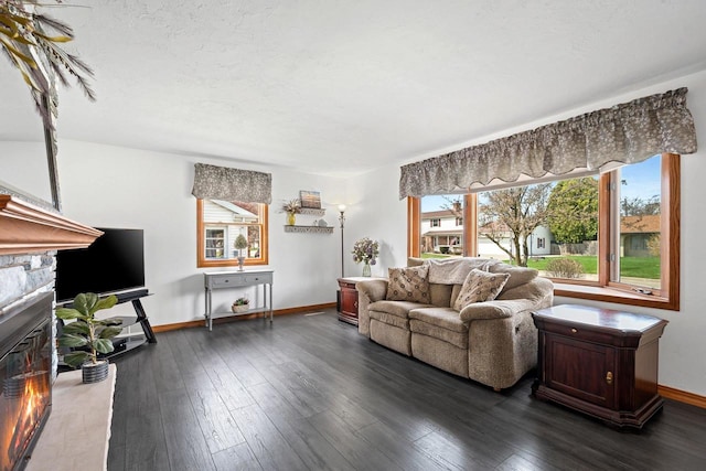 living area featuring baseboards, a glass covered fireplace, a healthy amount of sunlight, and dark wood-type flooring