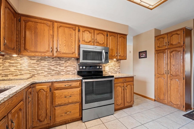 kitchen with brown cabinets, light tile patterned flooring, appliances with stainless steel finishes, and tasteful backsplash