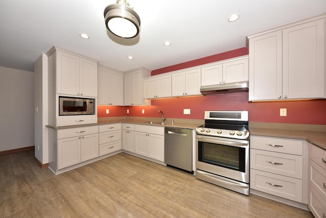 kitchen with light countertops, white cabinetry, under cabinet range hood, a sink, and appliances with stainless steel finishes