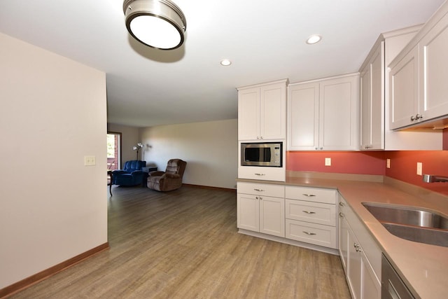 kitchen featuring white cabinetry, a sink, built in microwave, and light wood-style floors