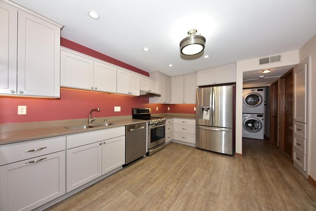 kitchen featuring visible vents, stacked washer and clothes dryer, a sink, light wood finished floors, and stainless steel appliances