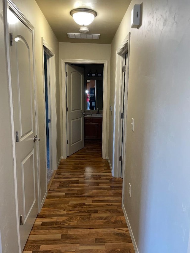 corridor with baseboards, visible vents, and dark wood-type flooring